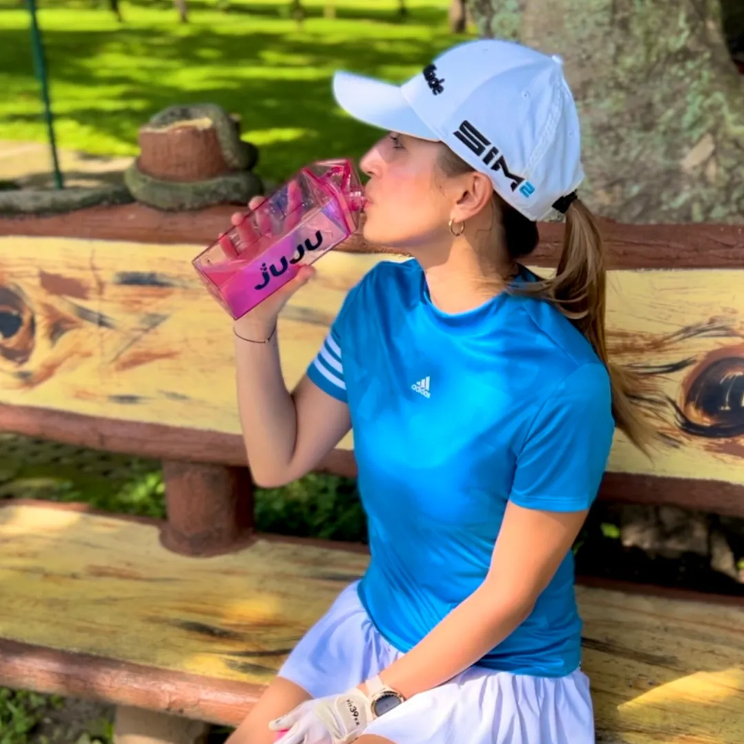Woman drinking from a pink JUJU bottle on a bench outdoors